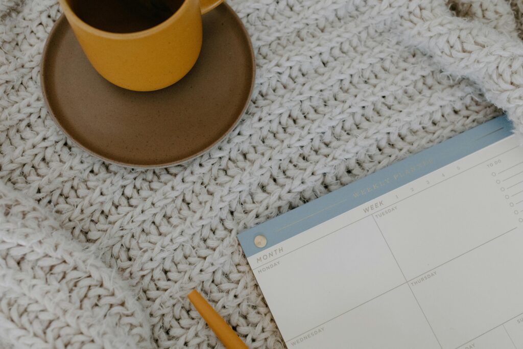 A warm coffee mug and weekly planner on a knitted blanket for a cozy morning vibe.